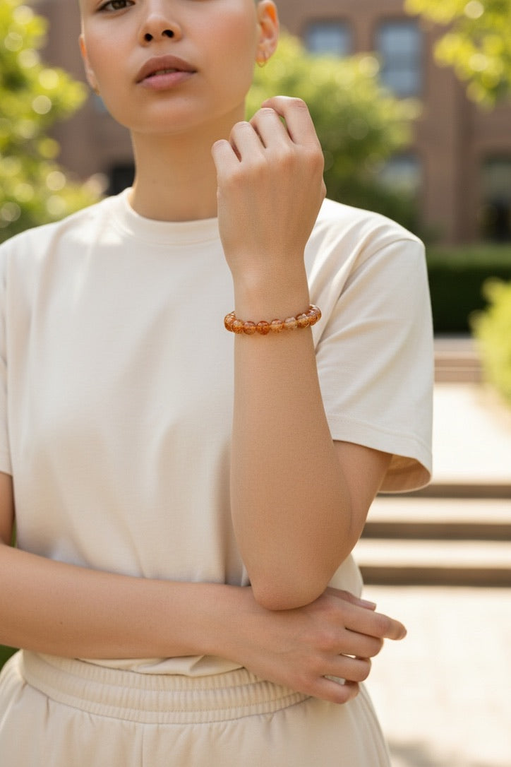 Woman wearing a bracelet outdoors with greenery and a building in the background