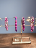 Pink beaded hoop earrings on a clear stand against a blue background