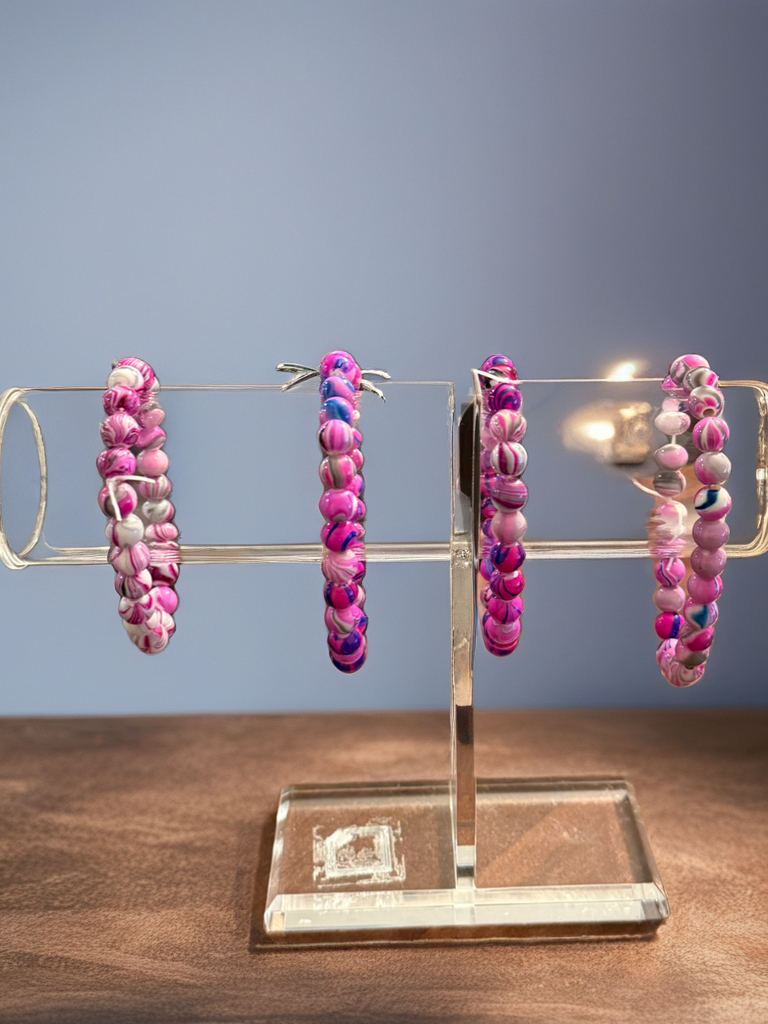 Pink beaded hoop earrings on a clear stand against a blue background