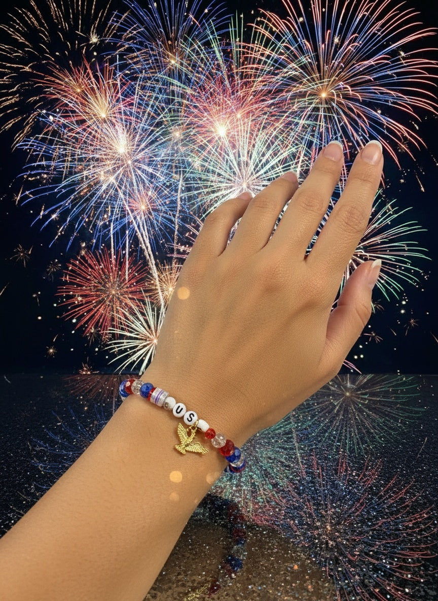 America’s Pride Bracelet with “USA” beads and gold eagle charm, shown against fireworks.