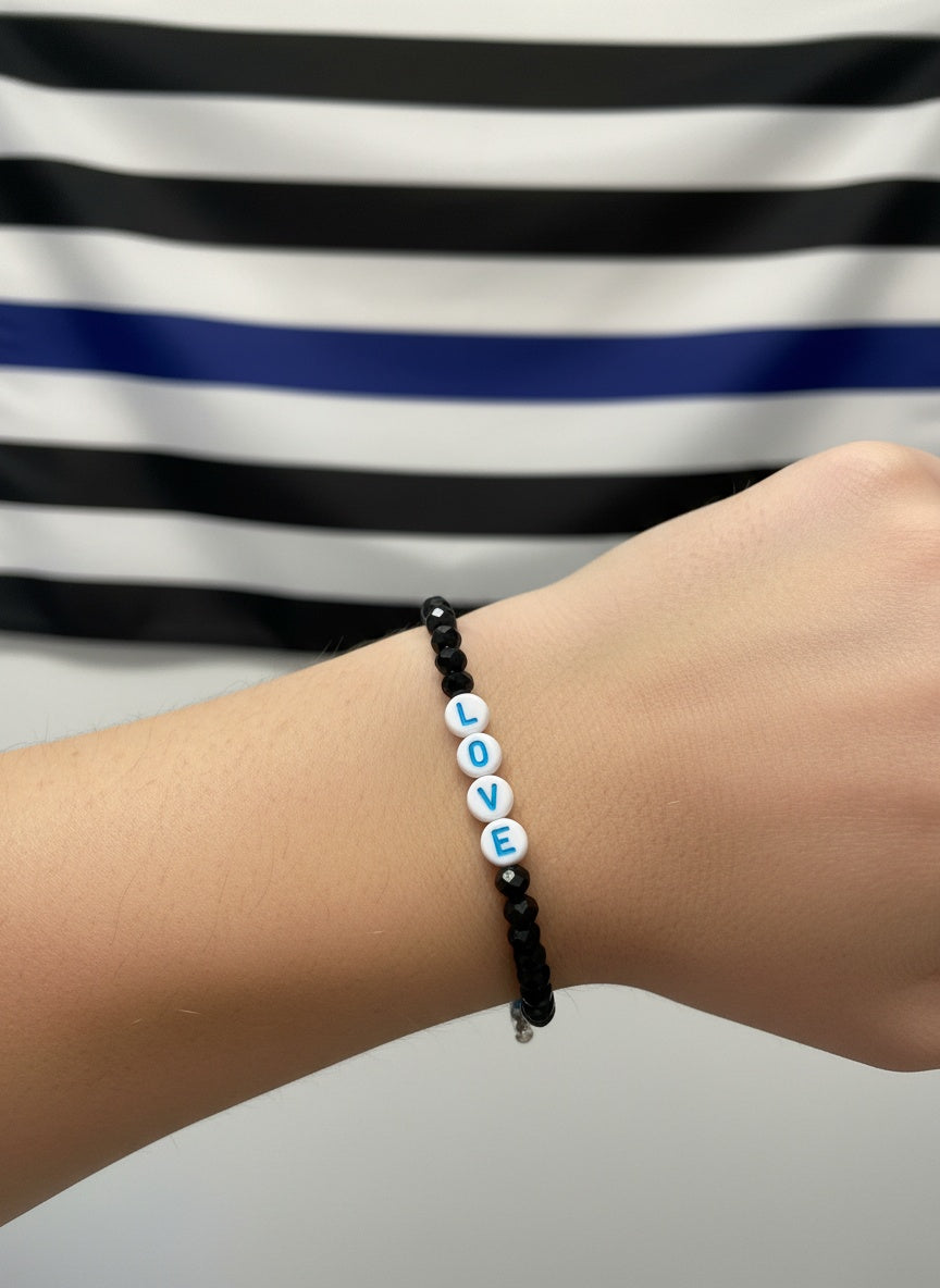 Hand wearing black beaded bracelet with white and blue “LOVE” letter beads.